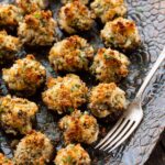 Angled view of crab stuffed mushroom appetizers with browned breadcrumb topping on a blue patterned serving platter beside a silver fork.