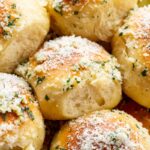 Close-up of soft garlic parmesan rolls with a golden crust, parmesan and parsley topping, and a pulled-apart roll showing the airy crumb.