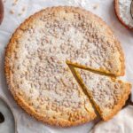 Overhead view of a powdered sugar-dusted pine nut custard tart with one slice cut and lifted slightly out on a vintage server.